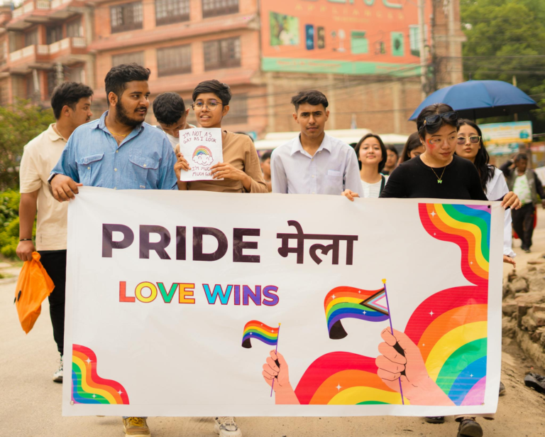 Diverse group holding Pride and Love Wins banner at a vibrant street march promoting LGBTQ+ rights.
