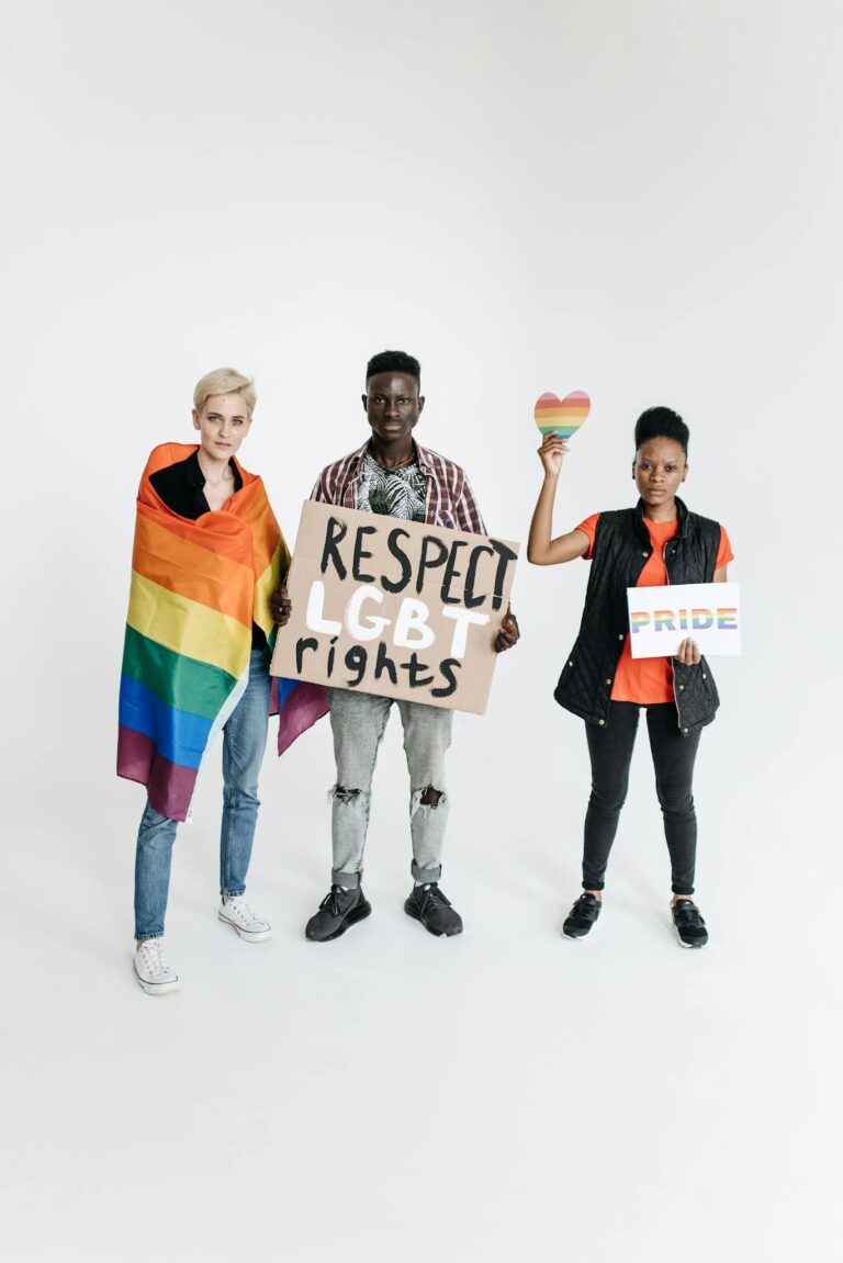 Three individuals stand together holding pride symbols and signs supporting LGBT rights.